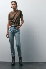 Pantalón de jean gris oscuro, de corte mom fit, tiro alto y largo tobillero. Cuenta con cinco bolsillos, cierre frontal con cremallera y botón.