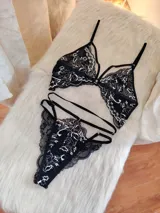 Conjunto de lencería negro con encaje bitono con detalles en color hueso. Incluye corpiño triangular de encaje con breteles ajustables y tanga con doble tira regulable en los laterales.