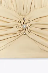 Top color crema con cuello halter, espalda descubierta, detalle de frunces y pieza metálica en forma de sol en el delantero.