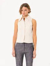 Camisa sin mangas confeccionada en tela de punto lisa, color crema, de corte regular. Lleva cartera con broches JCH y pinzas que entallan la prenda.