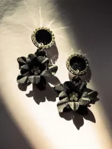 Par de aros colgantes con base circular negra con borde de strass y dije de flor negra con centro de strass.
