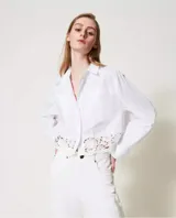 Camisa blanca de popelina de algodón con corte boxy y encaje macramé en el bajo. Presenta cuello clásico, manga larga con sisa caída, puños con abertura y botones, cierre con botones, bolsillos aplicados en la parte delantera y placa con logotipo Oval T en la parte trasera.