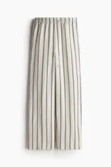 Pantalón de corte holgado en tejido liviano de mezcla de lino. Modelo de tiro alto con cintura elástica y cordón para ajustar fino, bolsillos laterales discretos y piernas rectas. Diseño a rayas verticales en blanco y negro.