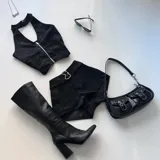 Conjunto de chaleco con cierre y shorts de cuero sintético negro con hebillas metálicas en forma de corazón. Incluye cartera baguette de cuero sintético negro con doble hebilla y botas de caña alta con taco bloque.