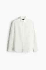 Camisa blanca de manga larga en mezcla de lyocell y algodón. Corte estándar, cuello inglés, tapeta clásica, bolsillo superior abierto, canesú con pliegue de caja en la espalda y bajo redondeado.