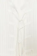 Camisa blanca a rayas verticales, de cuello redondo y manga larga con puños. Presenta cierre frontal con cordones ajustables con lazadas y abertura en la espalda ajustable con lazadas.