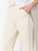 Pantalón color crema de corte slouchy con pinzas en las rodillas y bordados de hongos y chiles con strass.
