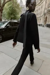 Blazer corta de color negro, entallada, sin solapa y con escote en V. Posee hombreras, cierre frontal de tres botones dorados y dos bolsillos delanteros con solapa.