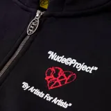 Campera negra con capucha, corte oversize y estampado de corazón roto con texto en la espalda. Incluye un sticker amarillo con texto manuscrito.
