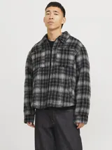 Sobrecamisa corta de manga larga con cuello sport, cierre frontal de cremallera, puños con botones, solapa cortaviento, bolsillos en pecho y delanteros. Diseño a cuadros grises y negros.