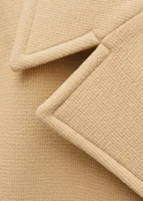 Abrigo corto color beige, de doble botonadura, con cuello con solapa y bolsillos laterales.