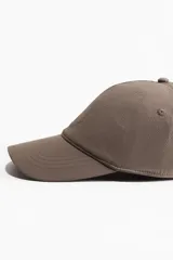 Gorra color marrón topo de sarga de algodón con diseño circular bordado en el frente, ojales bordados y cierre ajustable de plástico en la parte posterior.