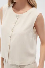Musculosa color crema de viscosa, sin mangas, corte holgado, con cuello a la base y cierre frontal con botones.