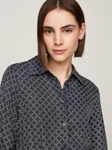 Vestido camisero midi azul marino con estampado geométrico en blanco, cuello camisero, manga larga con puños abotonados, cierre frontal con botones, cinturón de lazo y bajo asimétrico.
