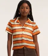 Blusa femenina de punto con cuello polo, mangas cortas y estampado a rayas en tonos naranja, marrón y blanco.
