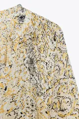 Blusa estampada con hilo metalizado, cuello redondo con volante, escote pico y manga larga abullonada.