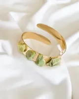 Brazalete rígido dorado con incrustaciones de piedra serpentina verde.