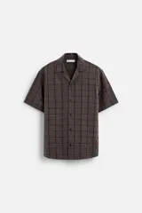 Camisa de hombre color gris con diseño a cuadros, corte relaxed fit, cuello bowling, manga corta y cierre frontal con botones.