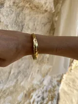 Brazalete rígido dorado con textura irregular.