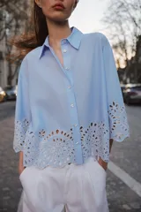 Camisa celeste de popelina con cuello solapa y manga ancha por debajo del codo. Bajo acabado con bordados perforados. Cierre frontal con botones.