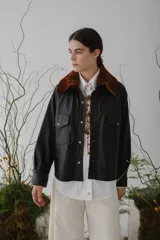 Campera corta de cuero color marrón con cuello de piel sintética color marrón claro, cierre frontal con botones a presión, mangas largas y bolsillos con solapa en el pecho.