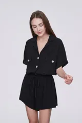 Mono corto negro con cuello camisero, cierre frontal con botones, mangas cortas, dos bolsillos con solapa en el pecho y cintura ajustable con cordón.