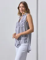 Blusa sin mangas con estampado a rayas verticales en tonos grises y blancos. Tiene cuello camisero, cierre frontal con botones y dos bolsillos con solapa en el pecho.