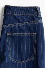 Jean de tiro superalto con pierna amplia y corte holgado. Presenta un diseño de cinco bolsillos, cierre con botón y un doblez ancho en el bajo que deja ver el revés de la tela. Confeccionado en denim con estampado de rayas finas verticales.