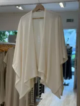 Ruana color crema de tejido calado, con corte asimétrico y terminación en punta.