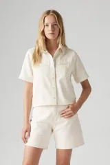 Camisa color crema de manga corta con cuello clásico, cierre frontal con botones y dos bolsillos con solapa en el pecho.