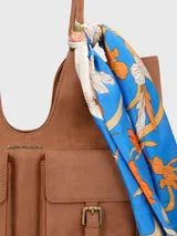 Cartera de hombro de ecocuero color gris, con compartimento principal con cierre cremallera, dos bolsillos frontales con solapa y broche imantado, bolsillo interior con cierre y bolsillo trasero con cierre. Incluye un pañuelo estampado como adorno.