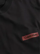 Remera negra de corte relaxed, cuello redondo y manga corta. Presenta un parche con el logo de Calvin Klein en el pecho.