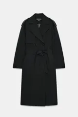 Gabardina larga color negro, estilo trench coat, con cuello solapa, cierre cruzado con botones y cinturón a tono anudado. Presenta trabillas en los hombros y bolsillos delanteros de vivo.