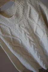 Sweater color crudo tejido a mano en lana merino, con diseño de trenzas en el frente.