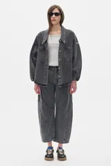 Camisa de jean oversized, color gris oscuro, con escote en V bajo, cuello camisero y mangas abullonadas. Tiene bolsillos delanteros y cierre con botones metálicos.