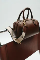 Bolso marrón formato city con asa doble de mano con detalles metálicos y correa interior extraíble en tejido canvas con posición bandolera. Bolsillo interior con cierre mediante cremallera metálica.