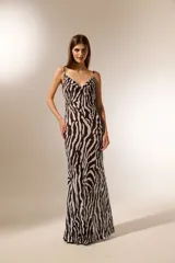 Vestido largo de poliéster con estampado animal print de cebra en blanco y negro. Tiene breteles finos, escote drapeado y corte al cuerpo.