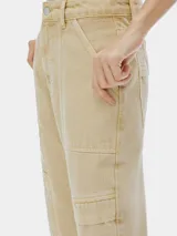 Pantalón cargo de mujer color beige claro, tiro medio/alto, con corte recto y detalles de costuras marcadas en el frente. Presenta bolsillos cargo amplios a la altura de los muslos.