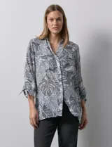 Camisa de mujer estampada con hojas en blanco y negro, cuello con solapa, abertura central con botones, bolsillos aplicados en el delantero y mangas largas con lazo.
