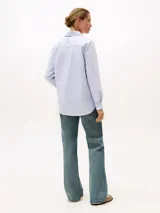 Camisa celeste a rayas verticales blancas, de corte amplio, con cuello inglés y logo bordado en el pecho.