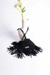 Cartera de hombro negra de gamuza con forma redonda y abundante flecos largos que rodean todo el contorno. Posee una placa metálica dorada con el nombre "Urban Haus" en el frente. Cuenta con correa ajustable de cuero negro.