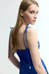 Vestido midi azul con breteles finos con moño y escote recto. Tiene broderie floral calado en todo el vestido y ribete festoneado en el escote y el ruedo.