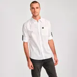 Camisa de popelina verde con cuello abotonado, cierre frontal con botones, bolsillo de parche en el pecho izquierdo, mangas largas con trabillas para enrollar y dobladillo camisero.
