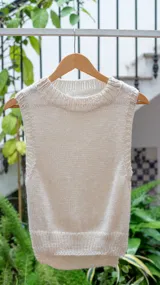Chaleco tejido color crema, con cuello alto y sin mangas.