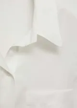 Camisa blanca sin mangas con cuello clásico, cierre frontal con botones y bolsillo de parche en el pecho.
