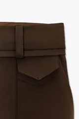 Shorts color marrón confeccionados en hilatura con algodón. Tiro alto y cintura doble con trabillas, bolsillos laterales y falso bolsillo con solapa en delantero. Detalle de costuras a contraste y cierre frontal con cremallera y ganchos metálicos.