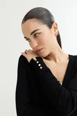 Cárdigan negro de tejido de punto fino con escote en V, cierre frontal con botones dorados y mangas largas con puños ajustados.