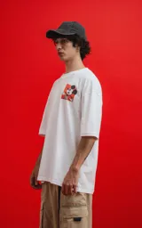 Remera blanca de algodón premium con cuello redondo y calce oversize. Presenta un pequeño estampado en el pecho izquierdo de Mickey Mouse en una pose dinámica sobre un fondo naranja.