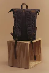 Mochila marrón de lona con detalles en cuero, cierre superior enrollable con hebillas y dos bolsillos frontales con hebilla.