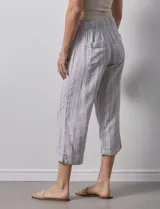 Pantalón capri de lino a rayas verticales en tonos grisáceos y beige, con cintura elástica y lazo ajustable.